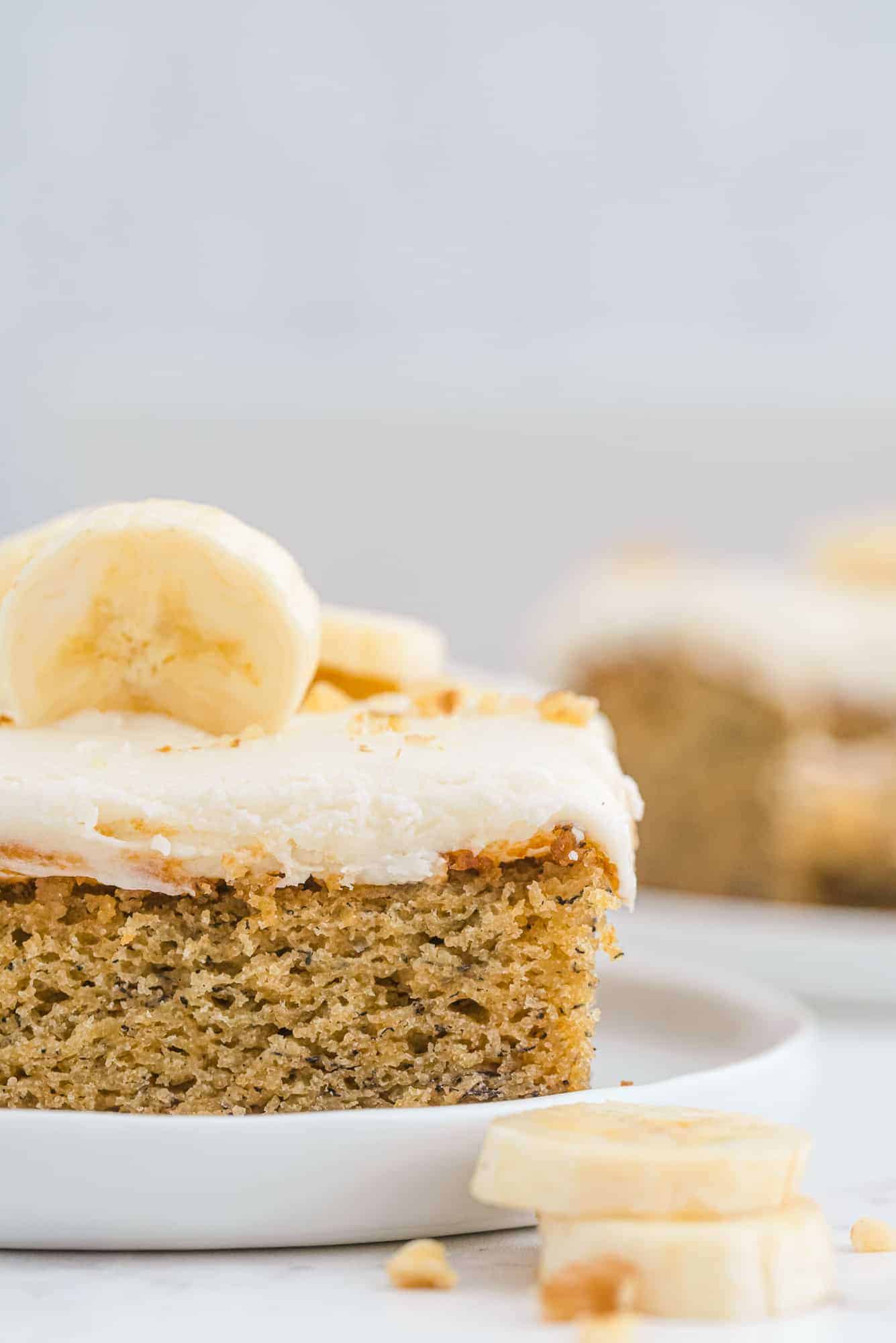 Square piece of banana cake with cream cheese frosting on a white plate.