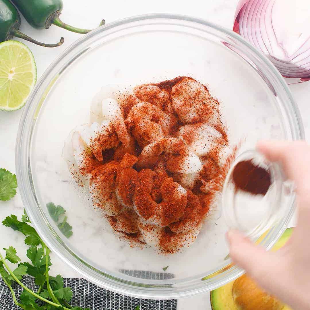 Spices being sprinkled over raw shrimp.