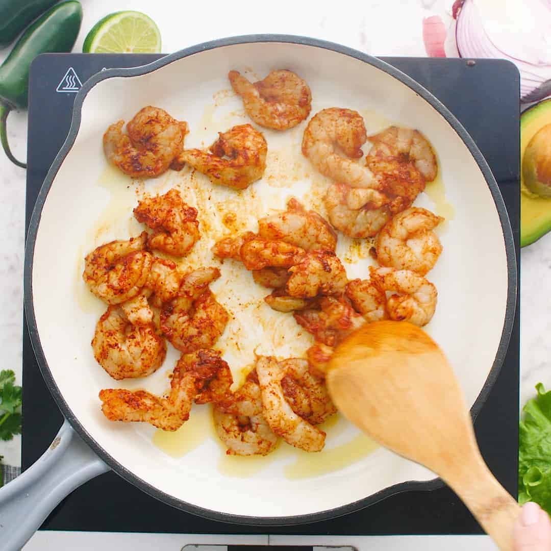 Shrimp cooking in a white skillet.