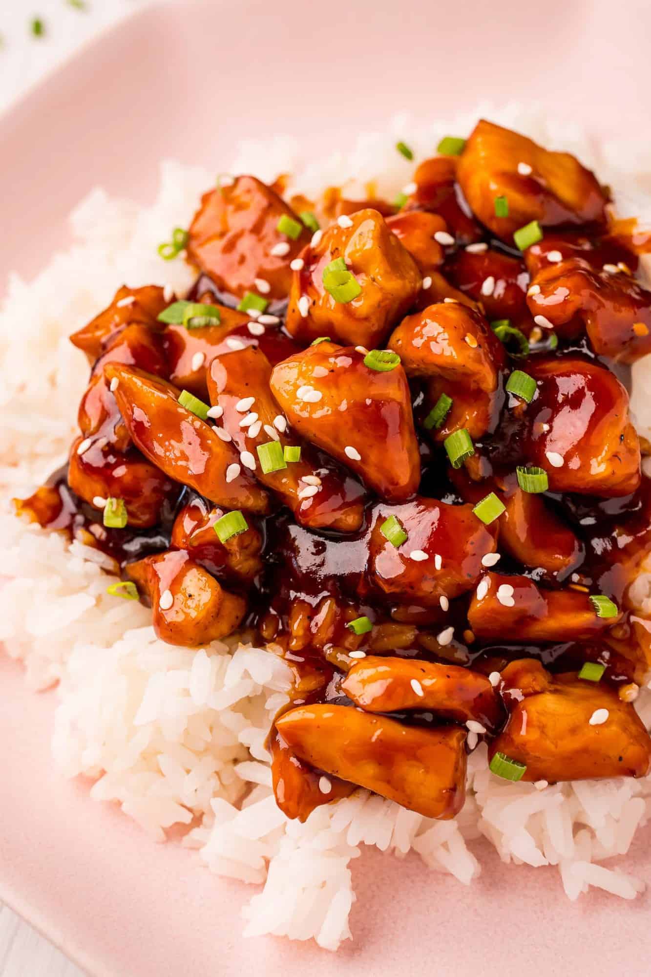 Close up of bourbon chicken on rice, topped with sesame seeds.