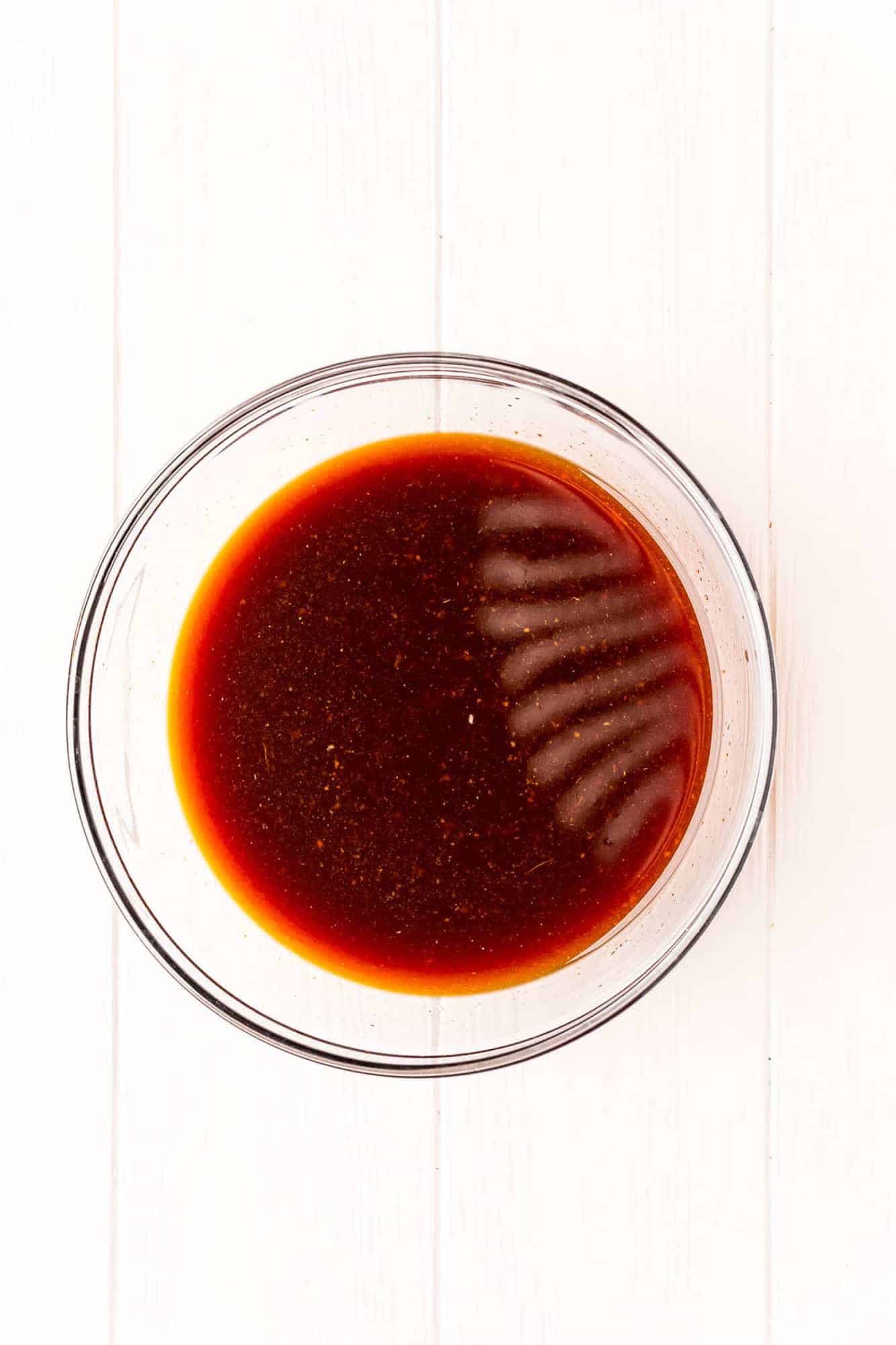 Dark brown sauce in a clear glass mixing bowl.