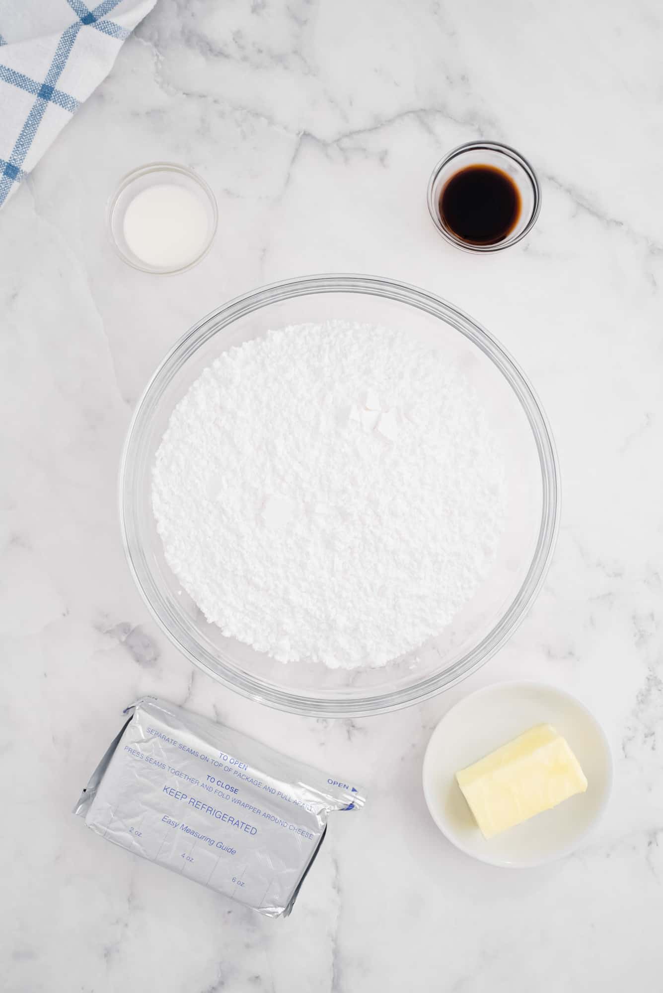 Overhead view of ingredients: Butter, cream cheese, powdered sugar, vanilla, and milk.