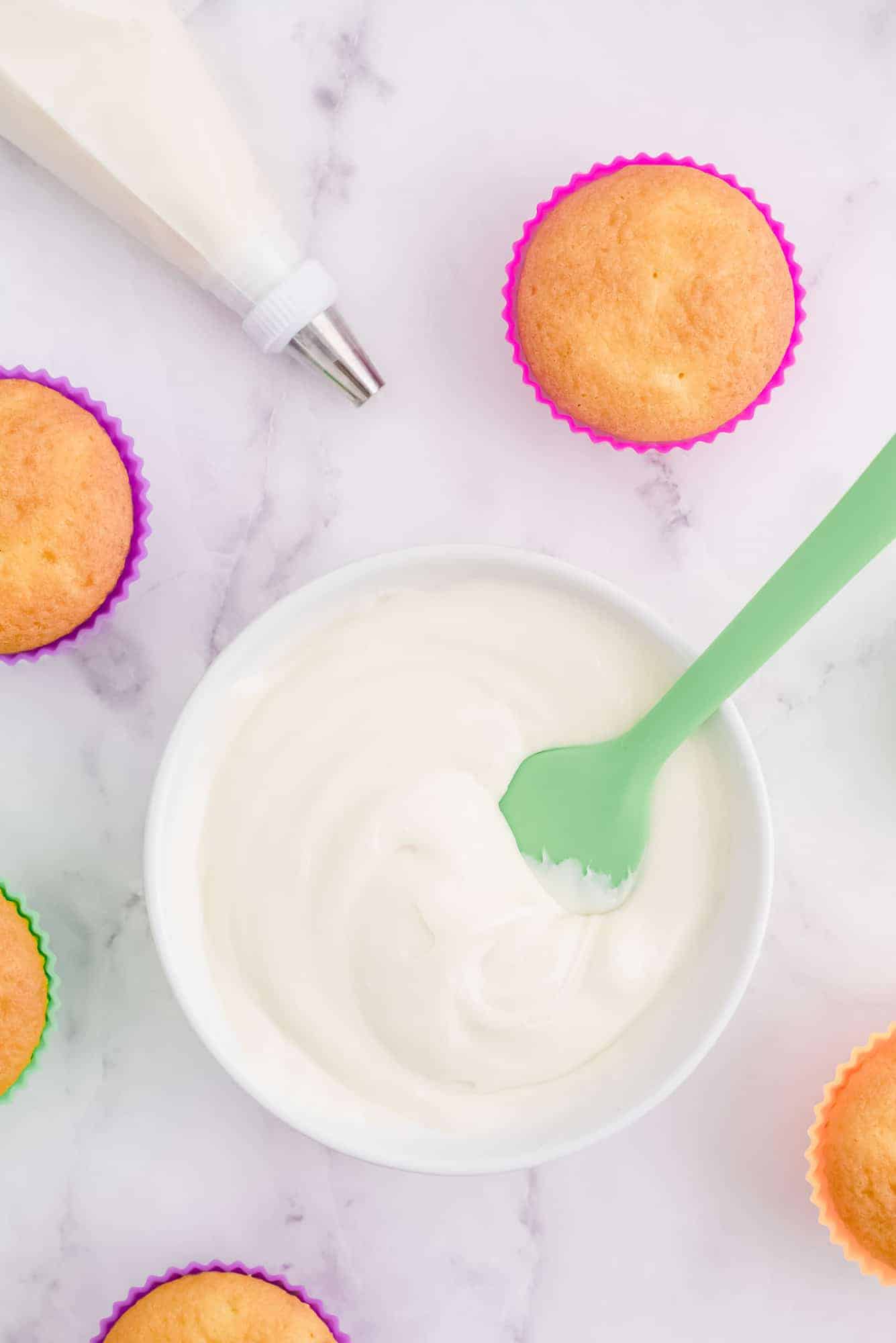 Overhead view of a bowl of frosting, bare cupcakes, and a piping bag.