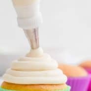 Frosting being piped on a cupcake, text overlay reads "the best homemade cream cheese frosting, rachelcooks.com"