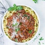 Overhead view of spaghetti and instant pot bolognese sauce in a white bowl, garnished with cheese and fresh basil.