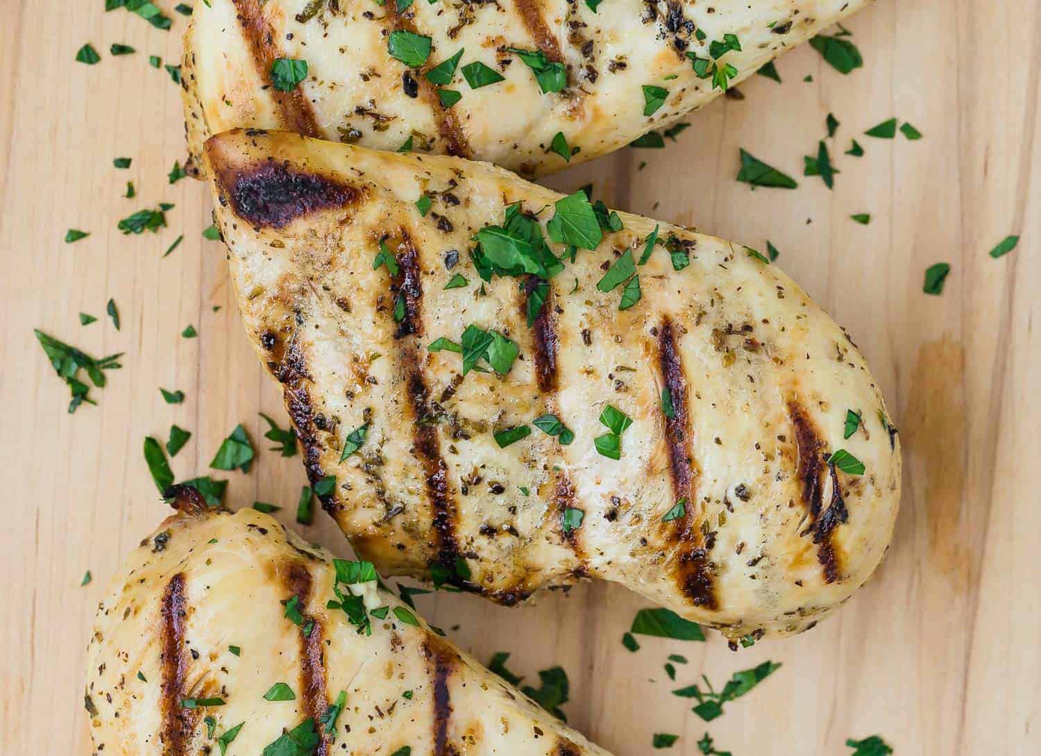 Close up view of a grilled chicken breast marinated in Italian chicken marinade. It is sprinkled with chopped fresh parsley.