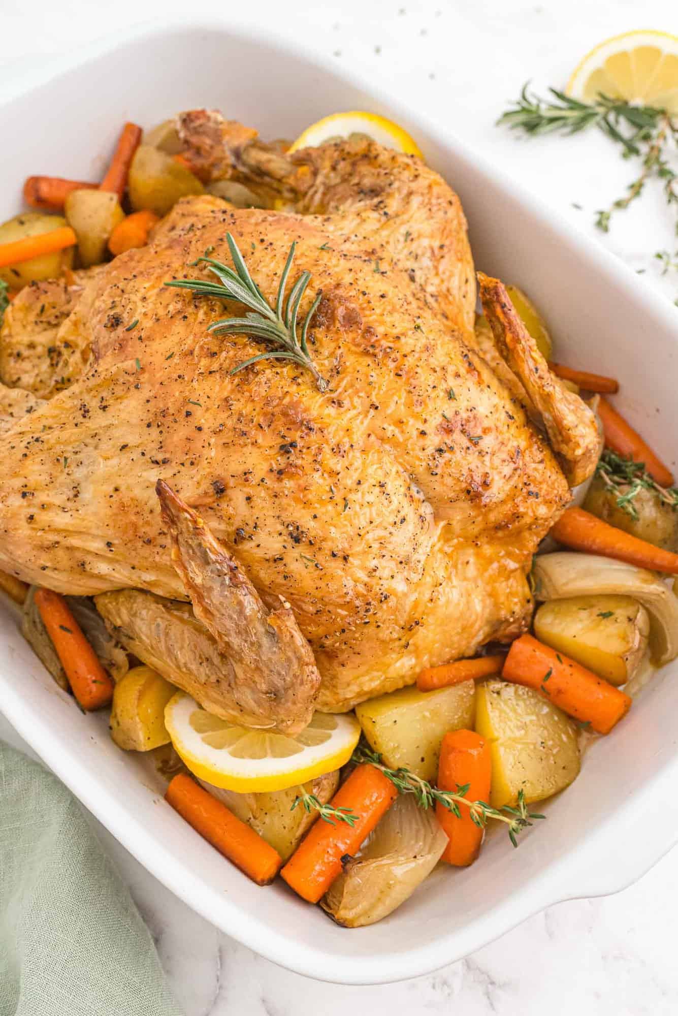 Roasted chicken with potatoes, onions, and carrots in a white baking dish.