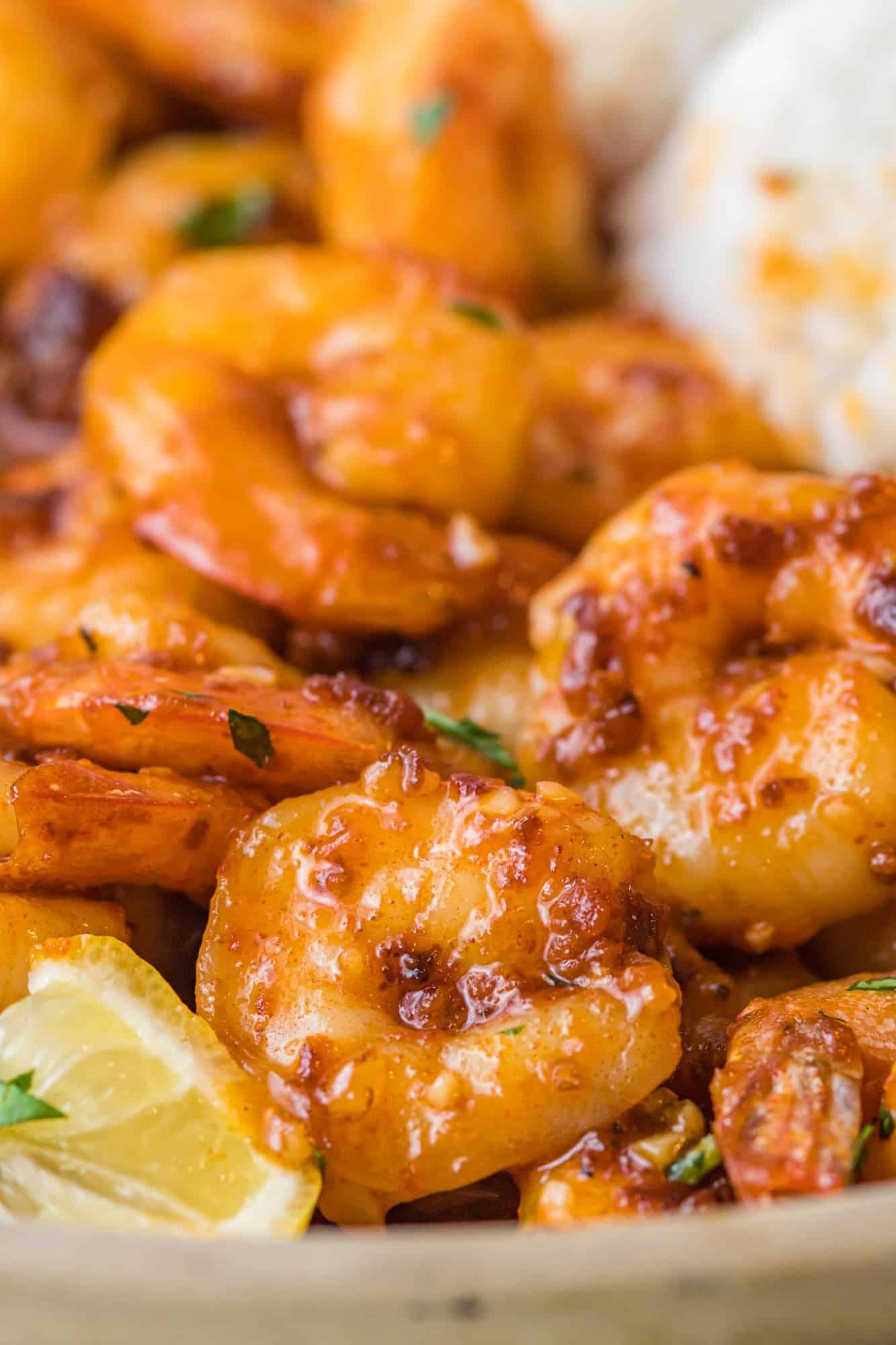 Close up of spicy honey garlic shrimp with lemon wedges and rice.