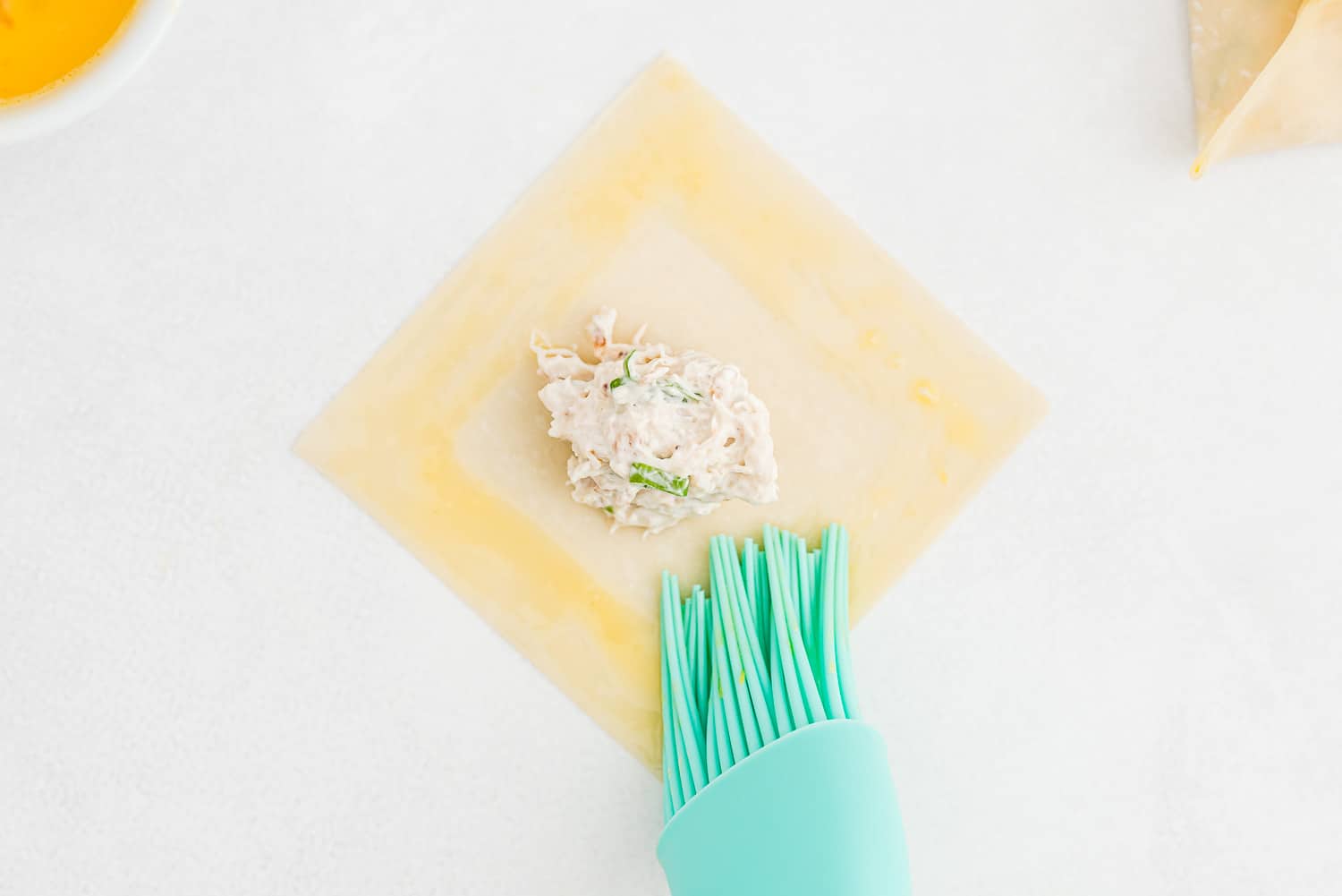 Egg wash being brushed onto a wonton wrapper.