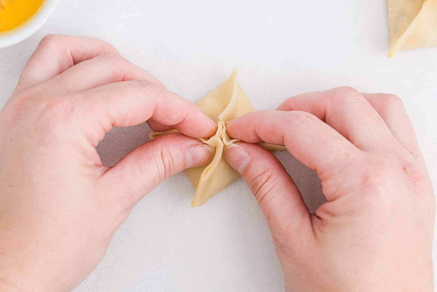 Two hands shown folding a rangoon.