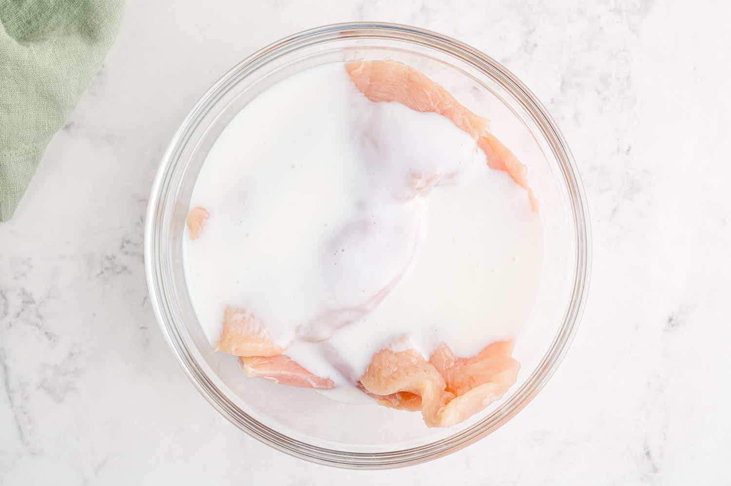 Raw chicken breasts soaking in buttermilk.