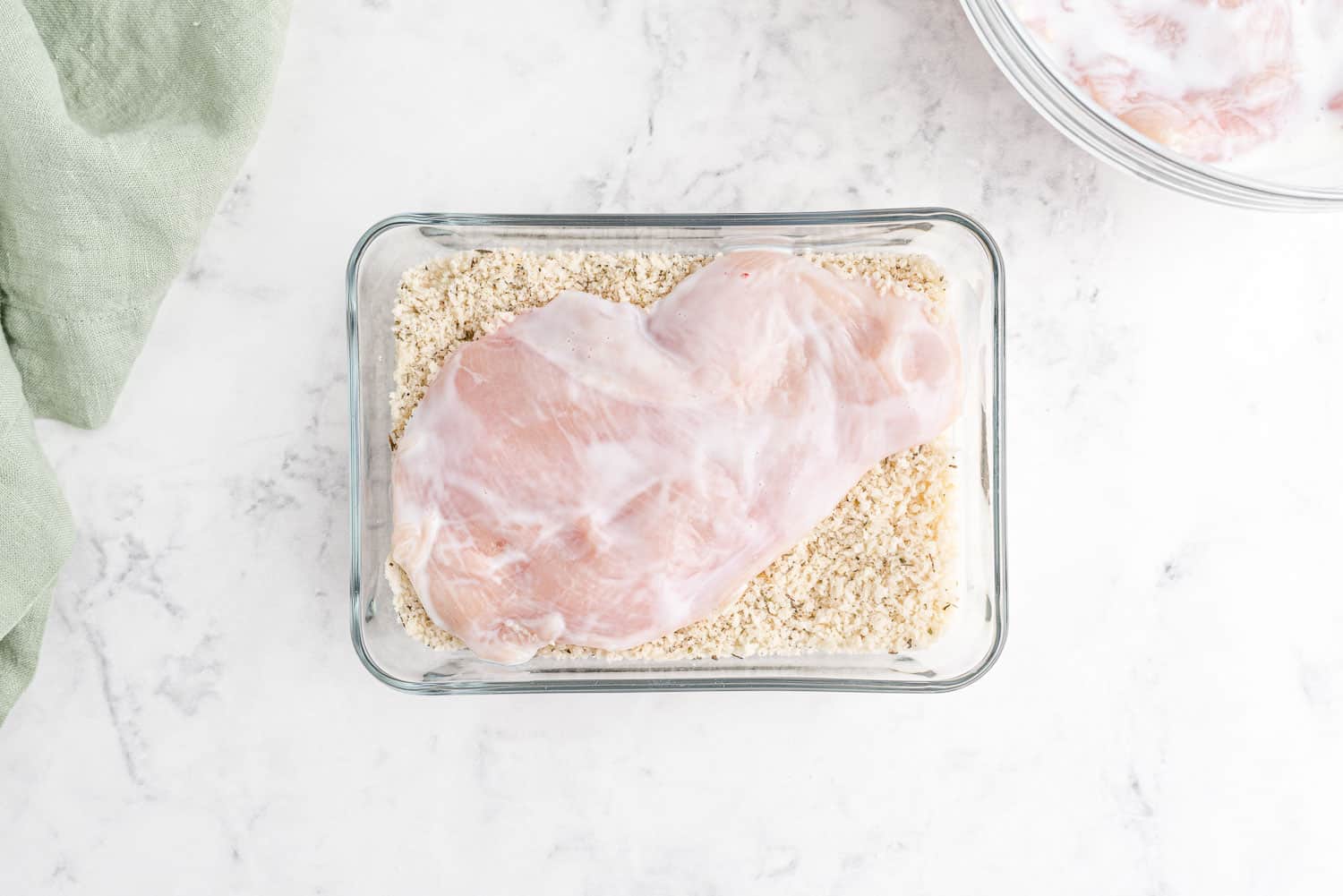 Chicken being dipped in bread crumbs.