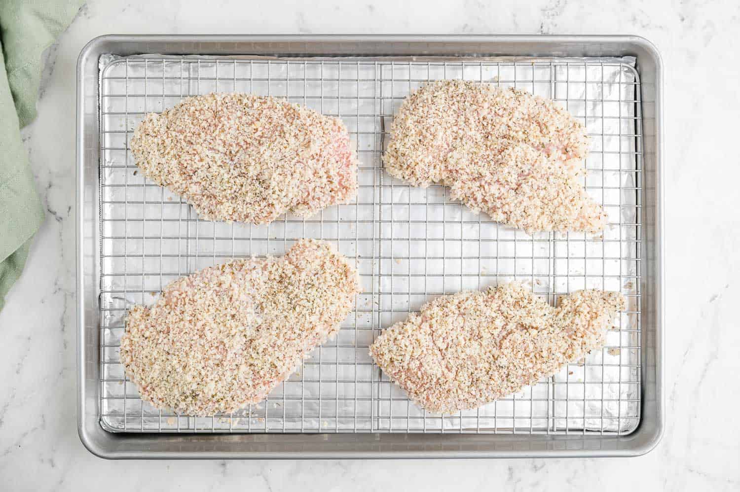 Breaded but uncooked chicken on a wire rack on top of a baking sheet.