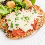 Chicken parmesan on a white plate with a green salad.