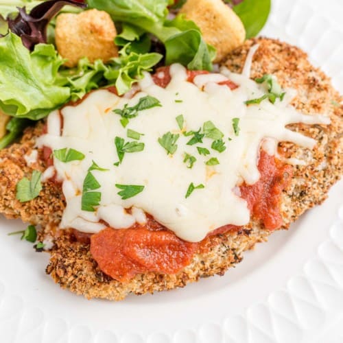 Chicken parmesan on a white plate with a green salad.