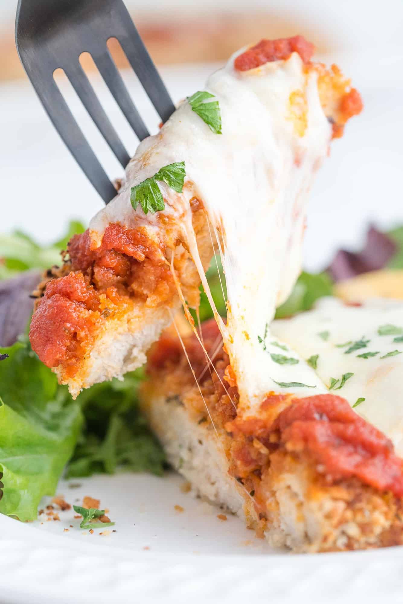 Close up of cheese pull on top of a breaded chicken breast.