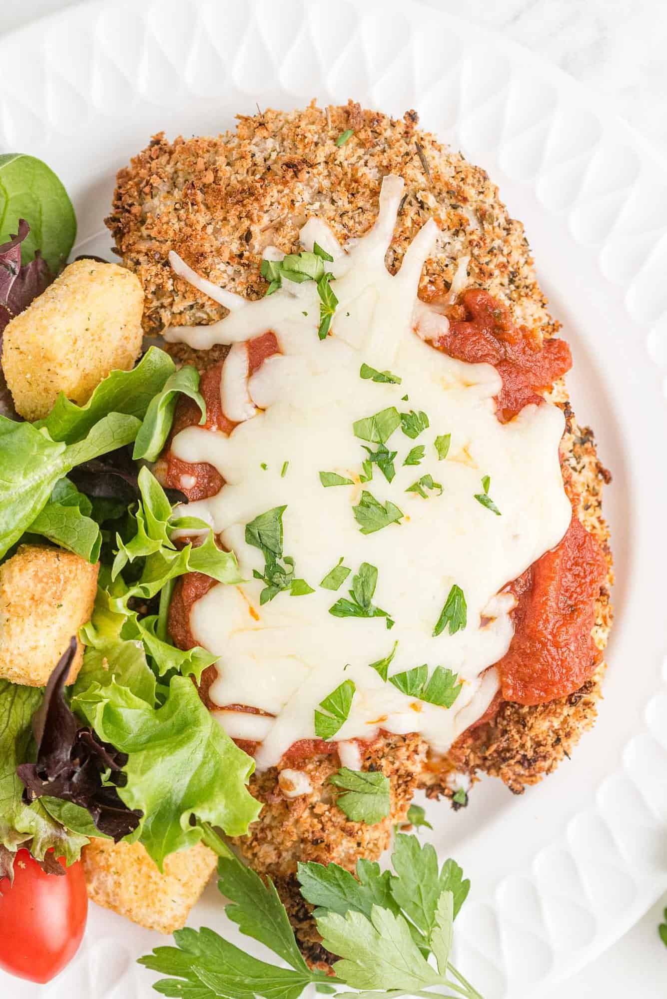 Chicken parmesan on a white plate with salad.