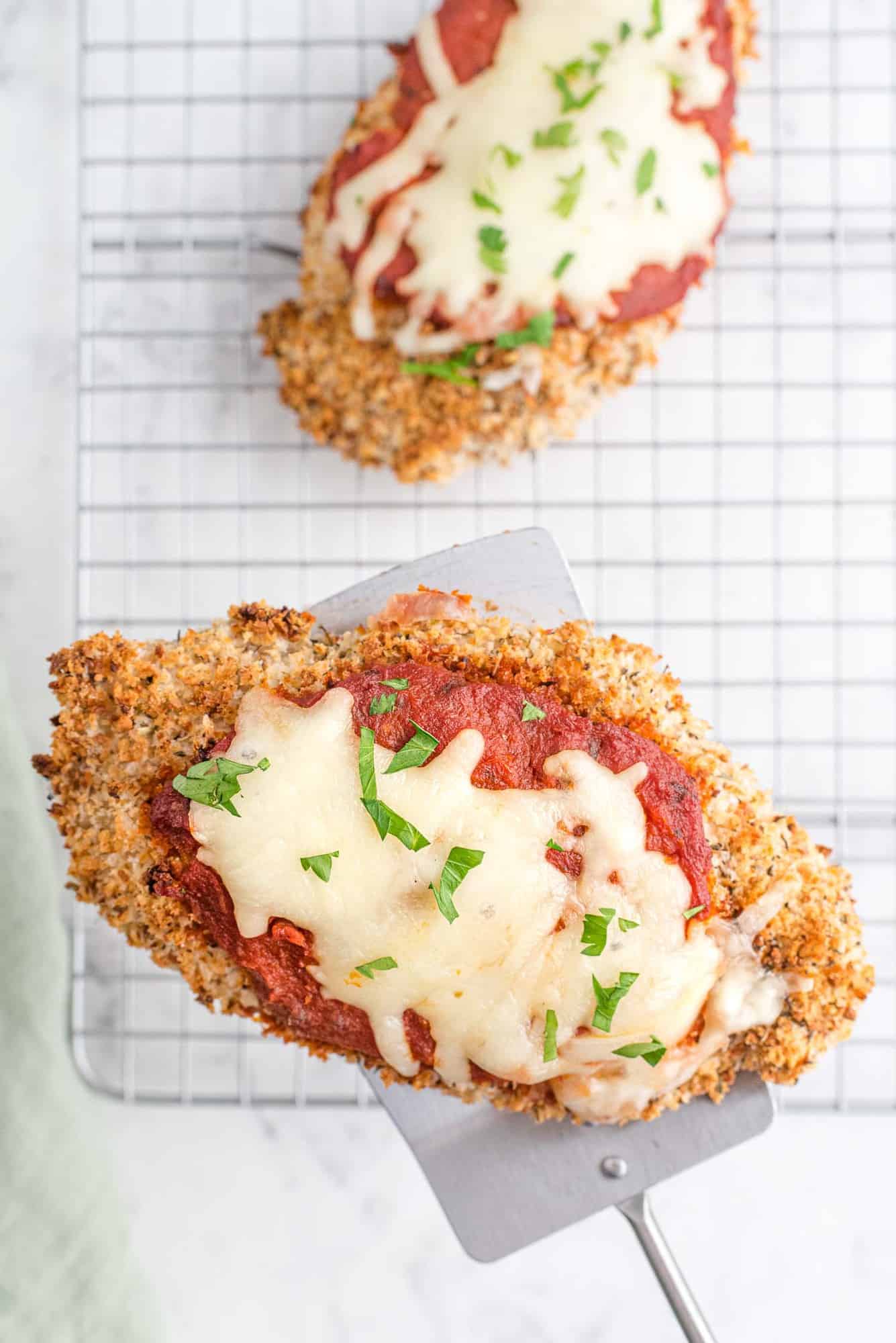 Chicken parmesan being taken off a metal baking rack with a metal spatula.