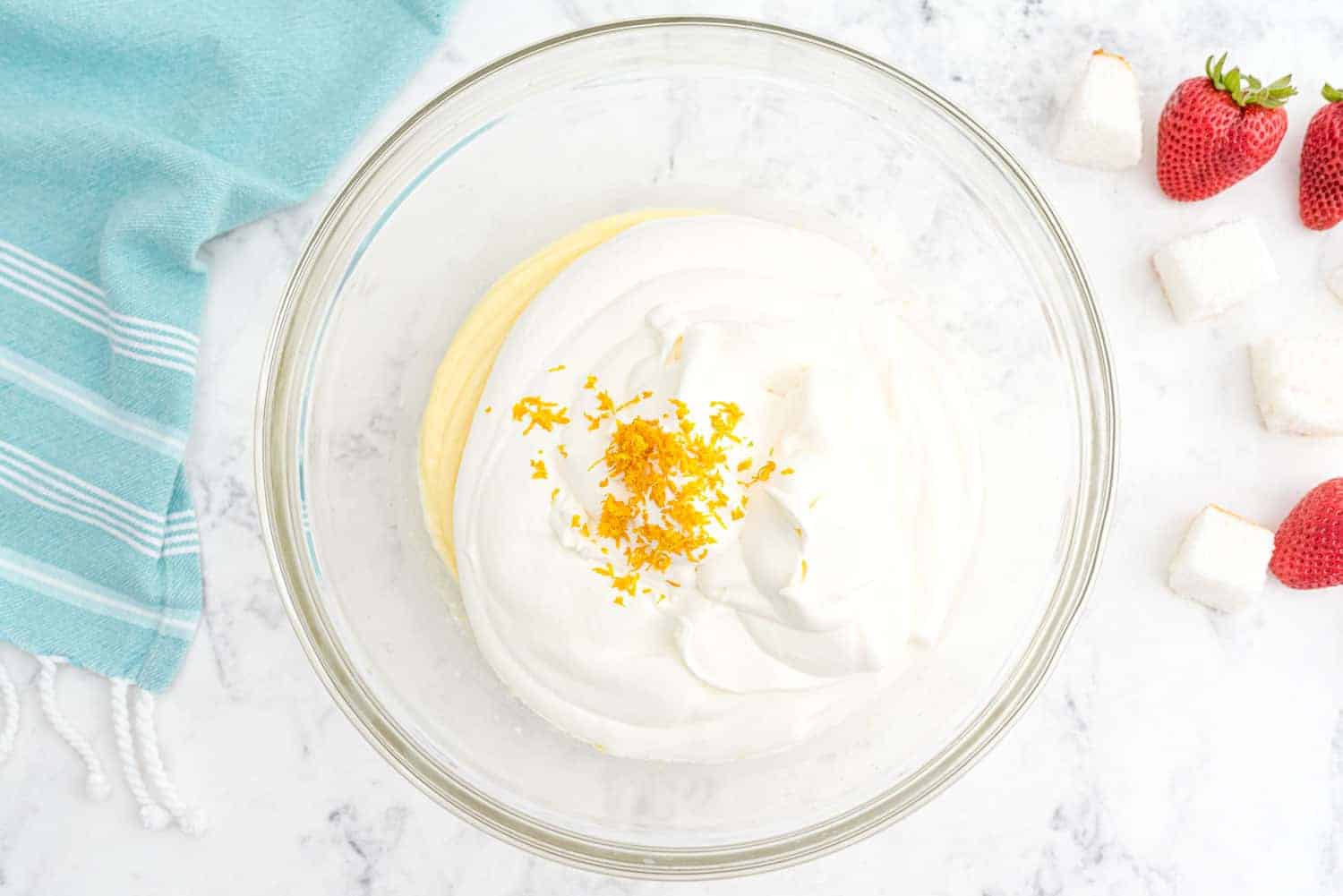 Pudding, whipped cream, and orange zest in a clear bowl.