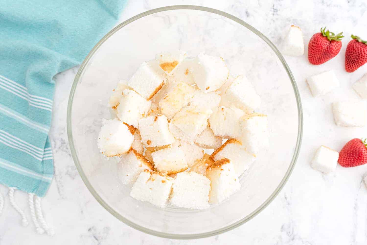 Cubed angel food in a clear glass mixing bowl.