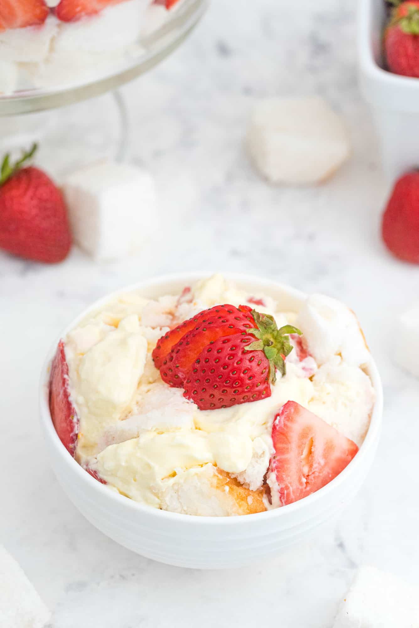 Trifle scooped into a small white bowl and topped with a strawberry.