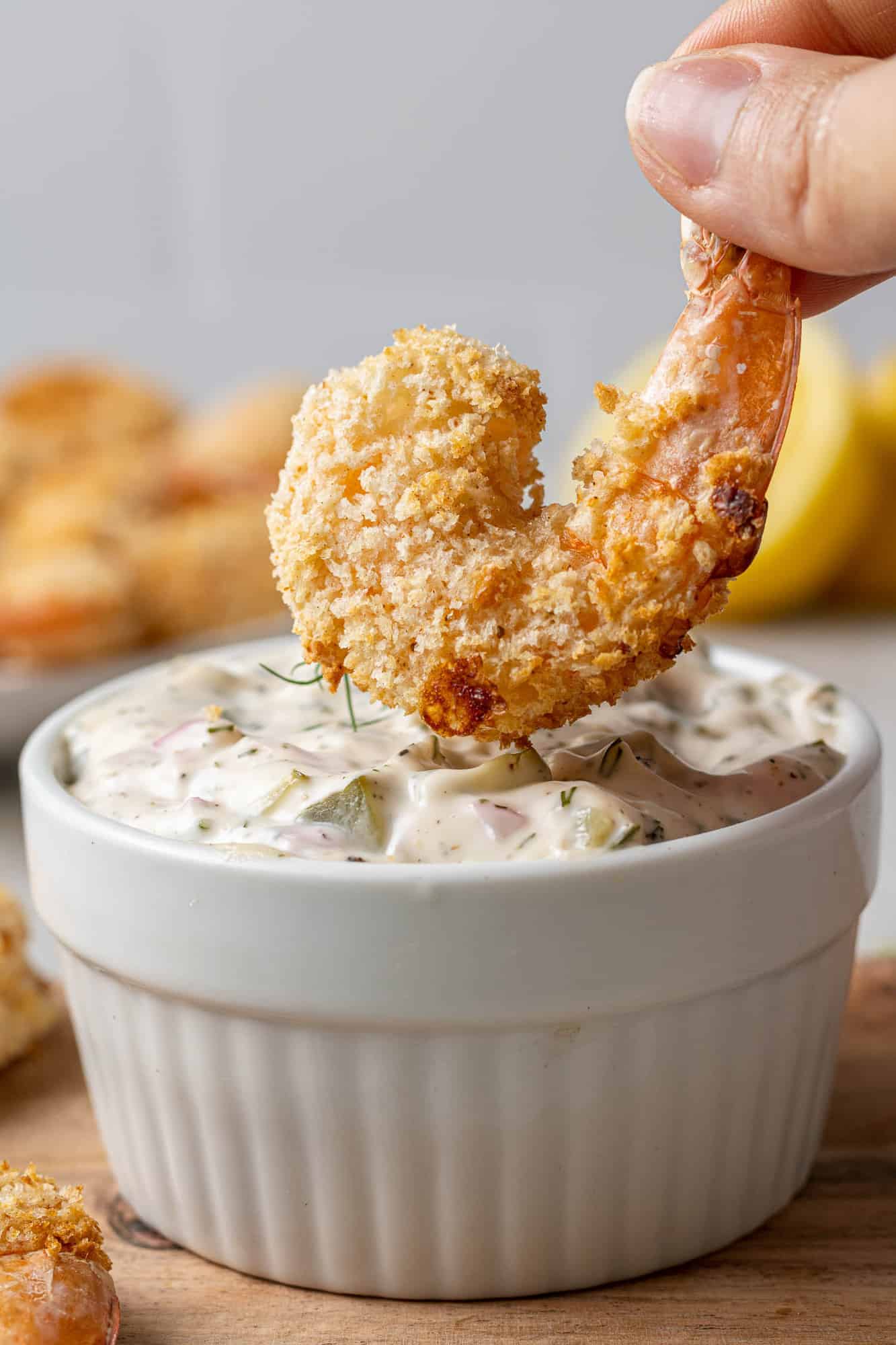 Breaded shrimp being dipped into tartar sauce.