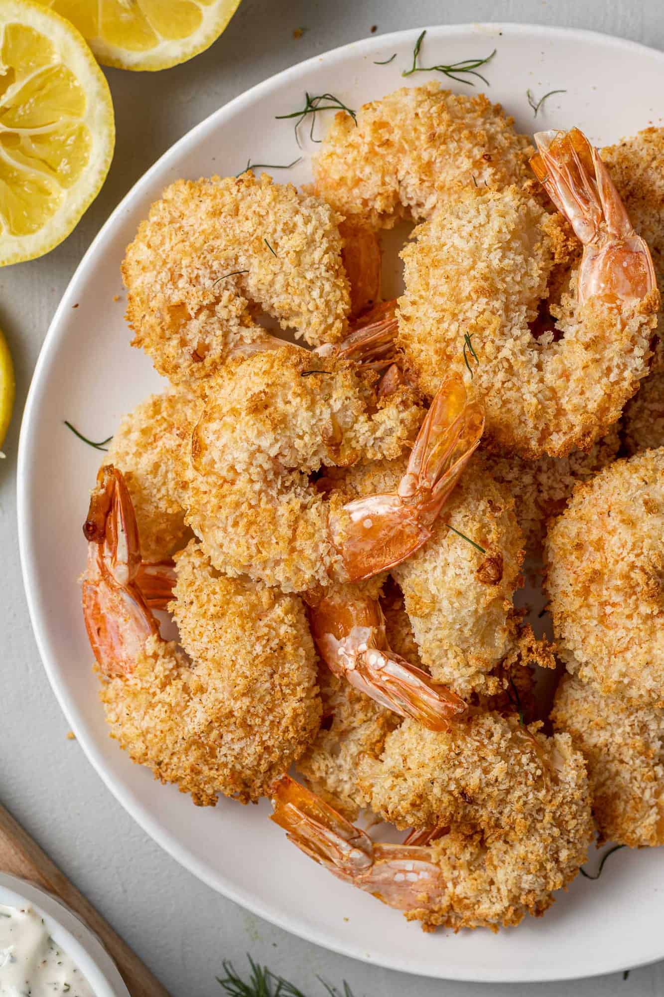 Breaded and cooked shrimp piled up on a white plate.