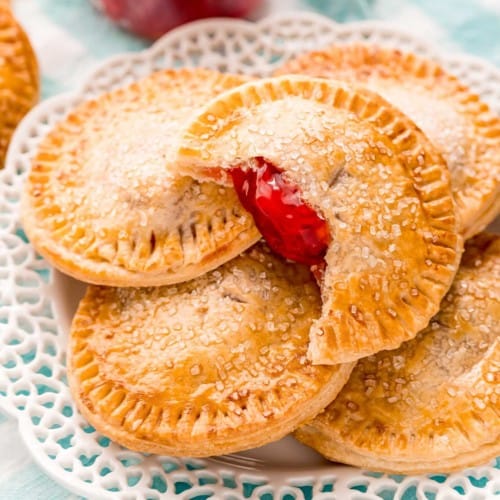 Pile of cherry hand pies on a white doily style plate.