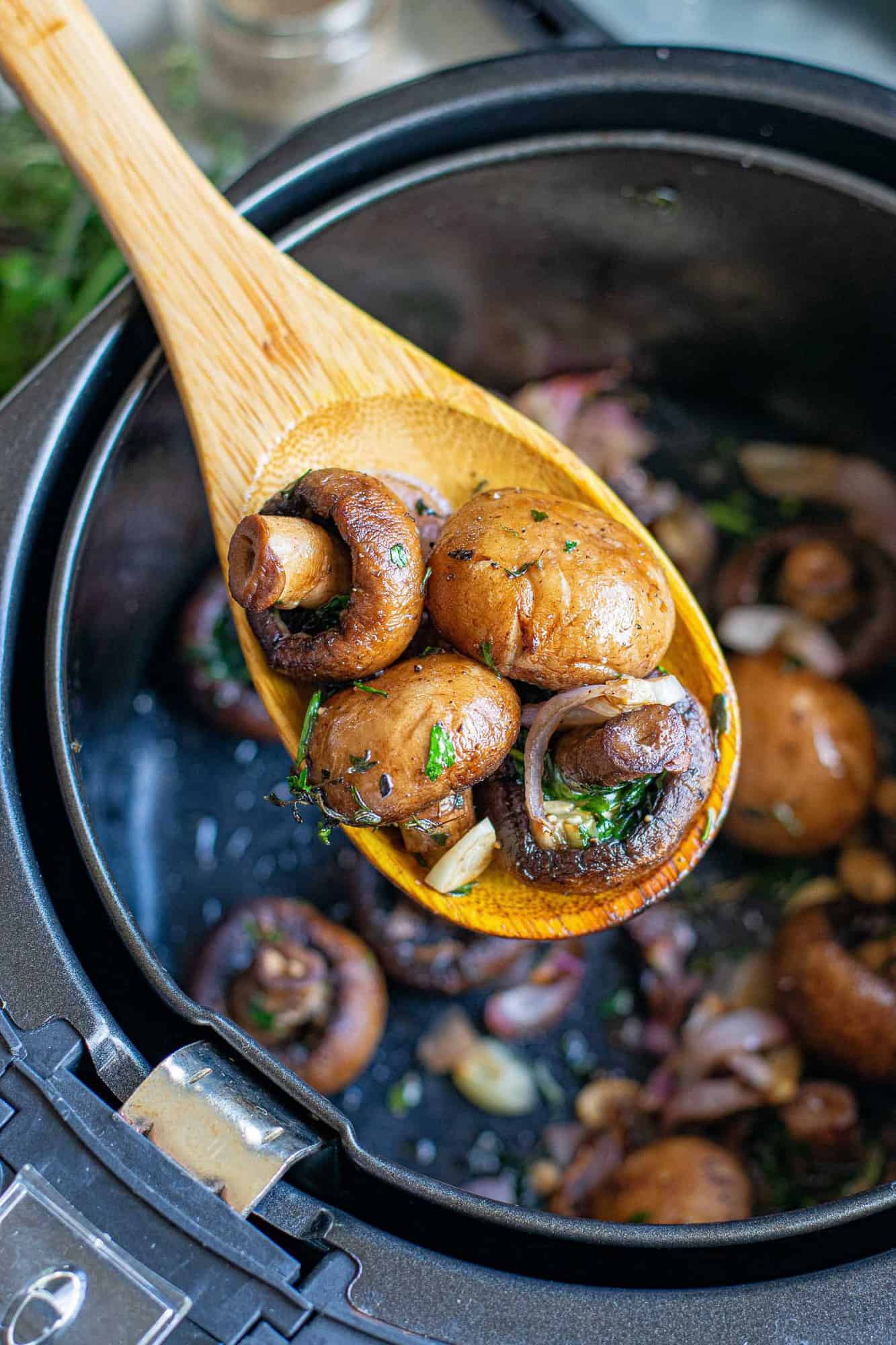 Cooked mushrooms being scooped out of an air fryer with a wooden spoon.
