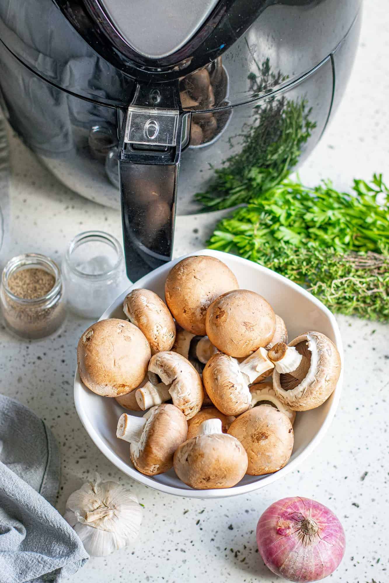 Air fryer, a bowl of fresh mushrooms, a shallot, and fresh herbs.