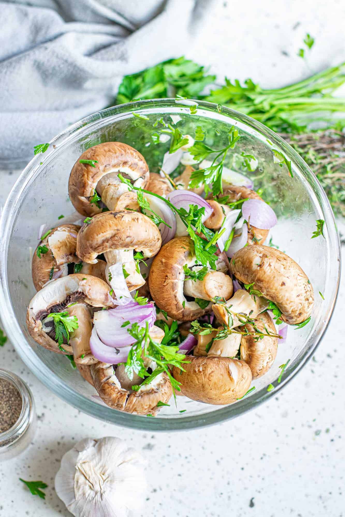 Uncooked mushrooms, shallot, garlic, and herbs in a bowl.