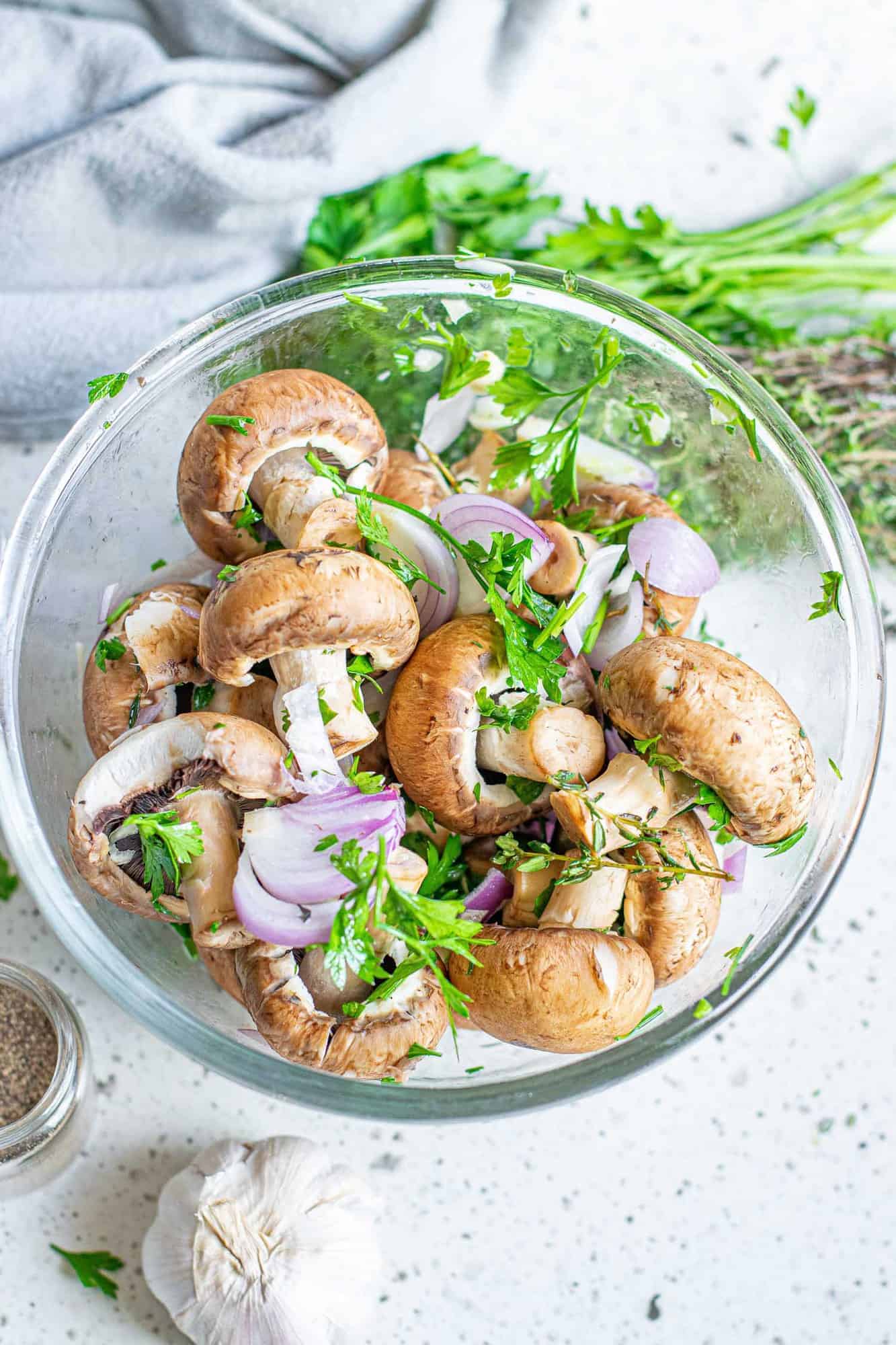Uncooked mushrooms, shallot, garlic, and herbs in a bowl.