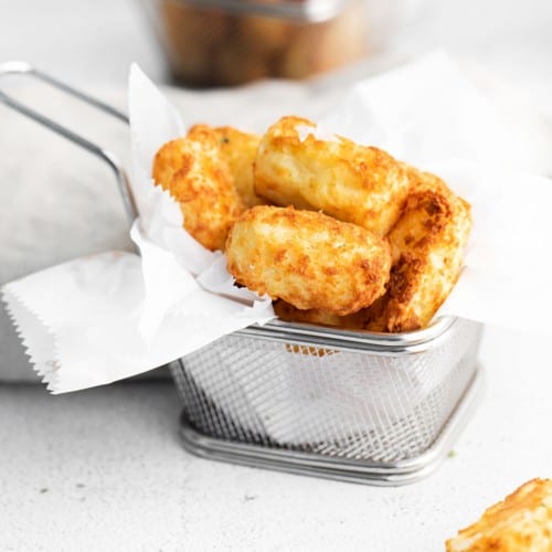 Air fryer tater tots in a tiny metal basket.