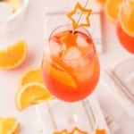 An light orange aperol spritz in a wine glass garnished with orange peel cut into the shape of a star.