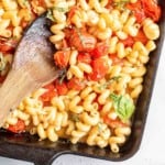 Pasta with feta and tomatoes, in a black baking dish with wooden spoon.
