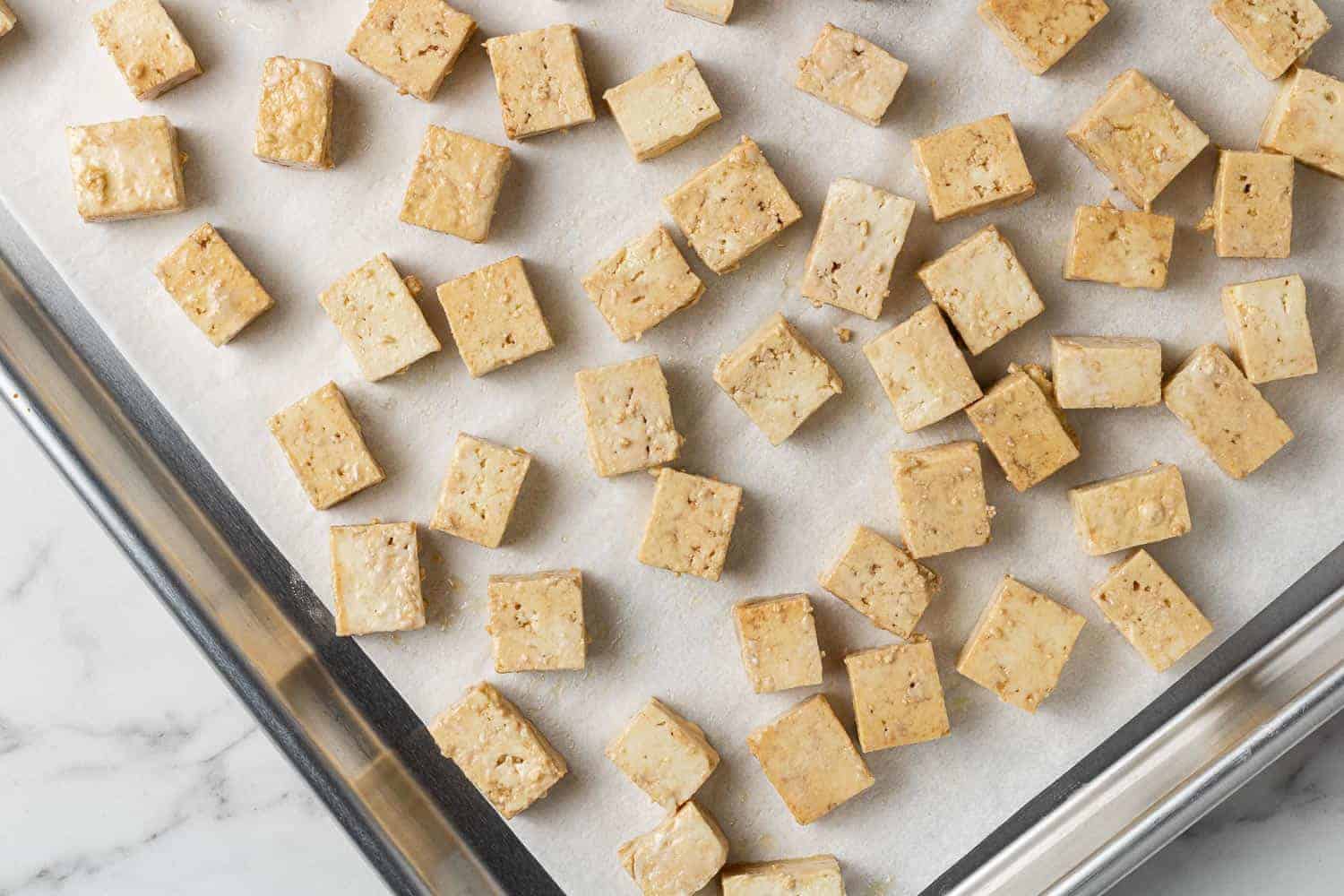 Unbaked tofu on a parchment paper lined baking sheet.