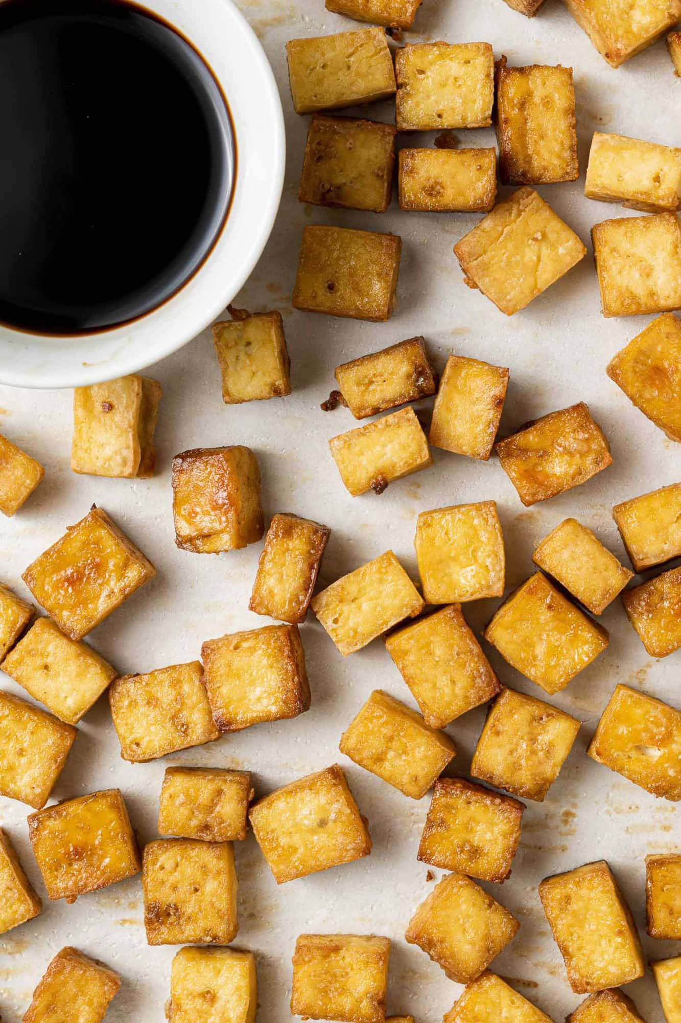 Overhead view of tofu on a baking sheet with a small bowl of soy sauce.