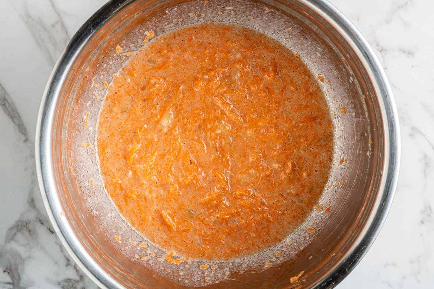 Wet ingredients and carrots in a metal mixing bowl.