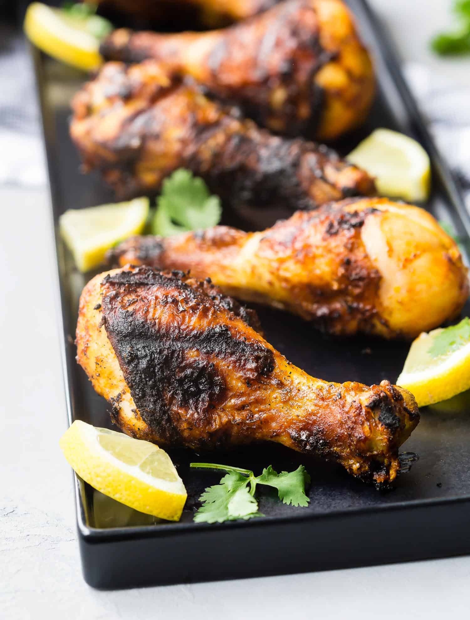 Drumsticks on a black platter with lemons.