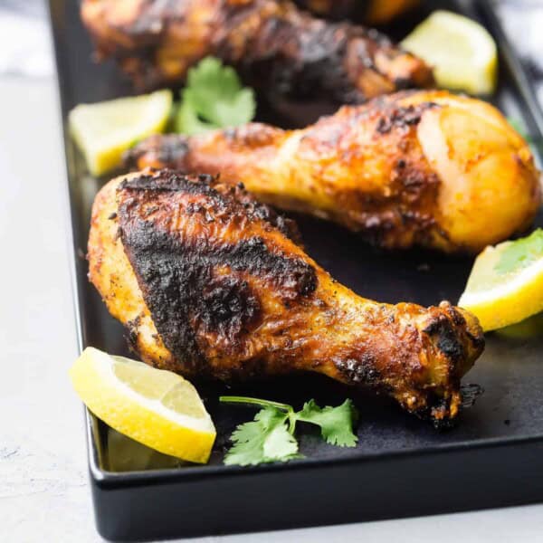 Grilled drumsticks on a black platter.