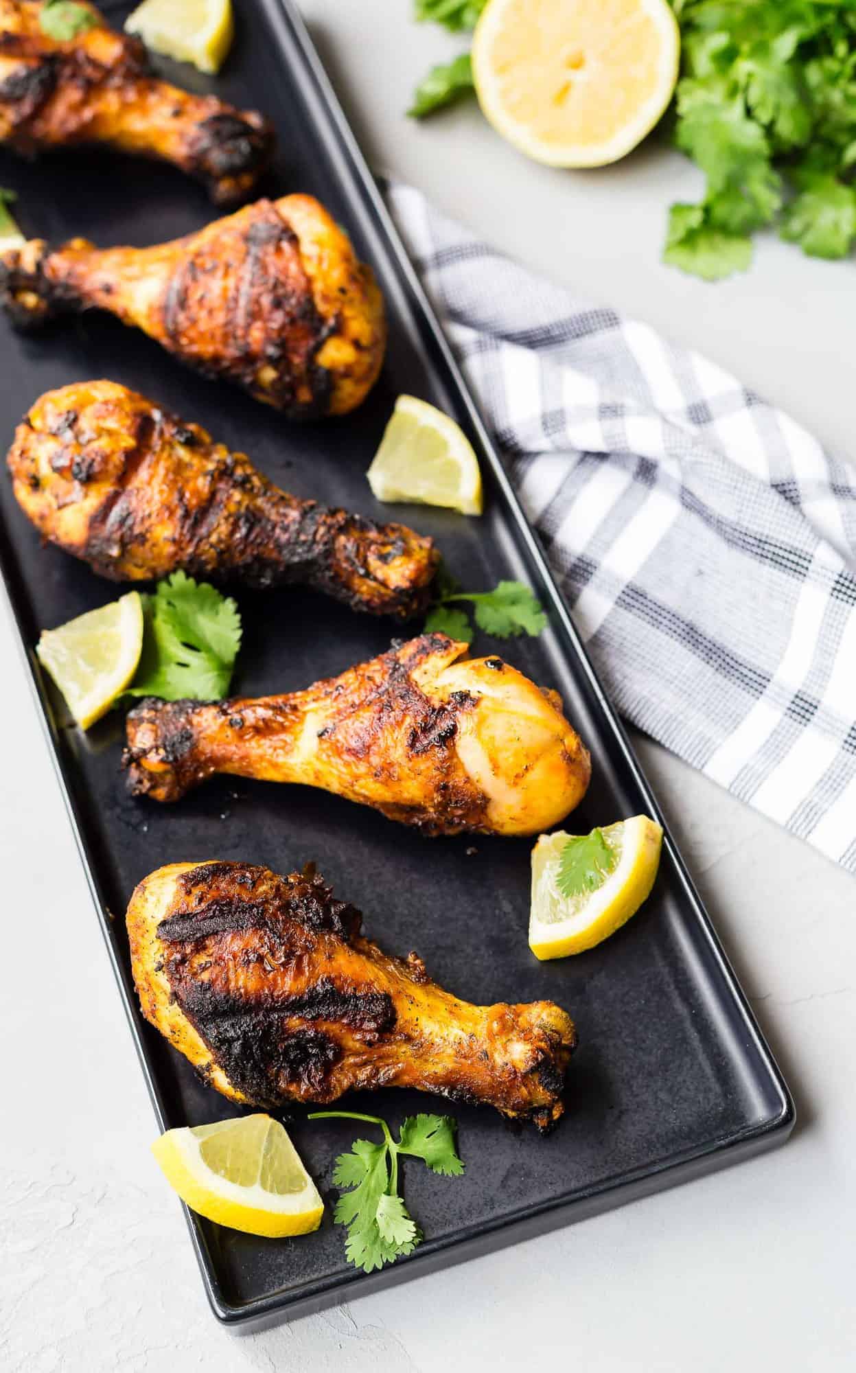Overhead view of rectangular black platter with grilled chicken drumsticks on it.
