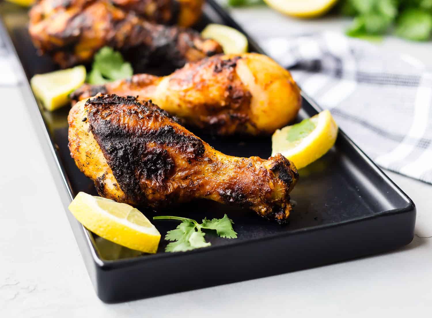 Grilled chicken drumsticks on a black platter with lemon slices and cilantro.