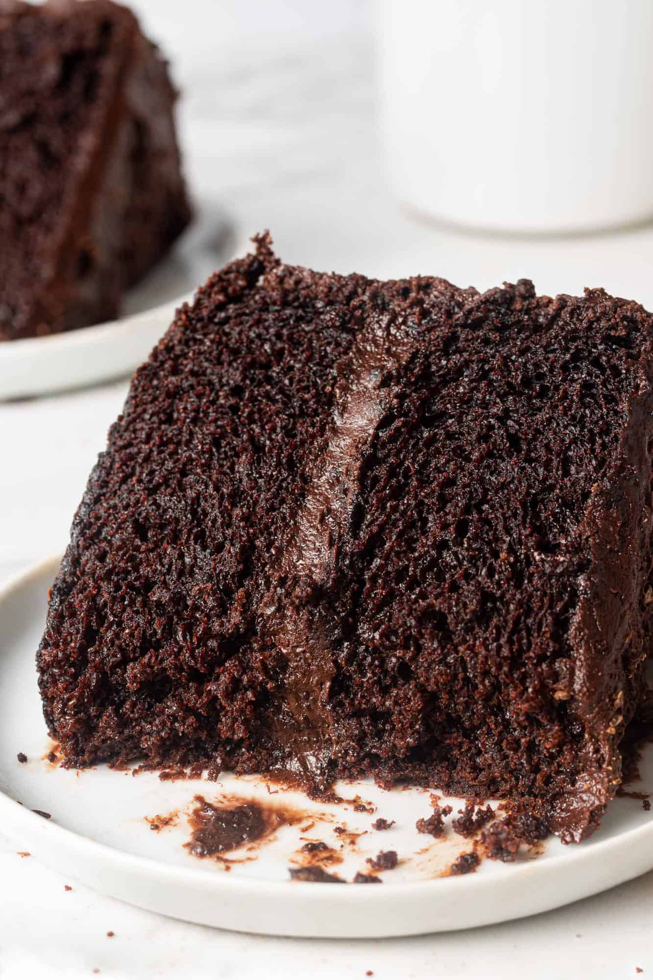 Slice of chocolate layer cake on a round white plate, with a bite removed.