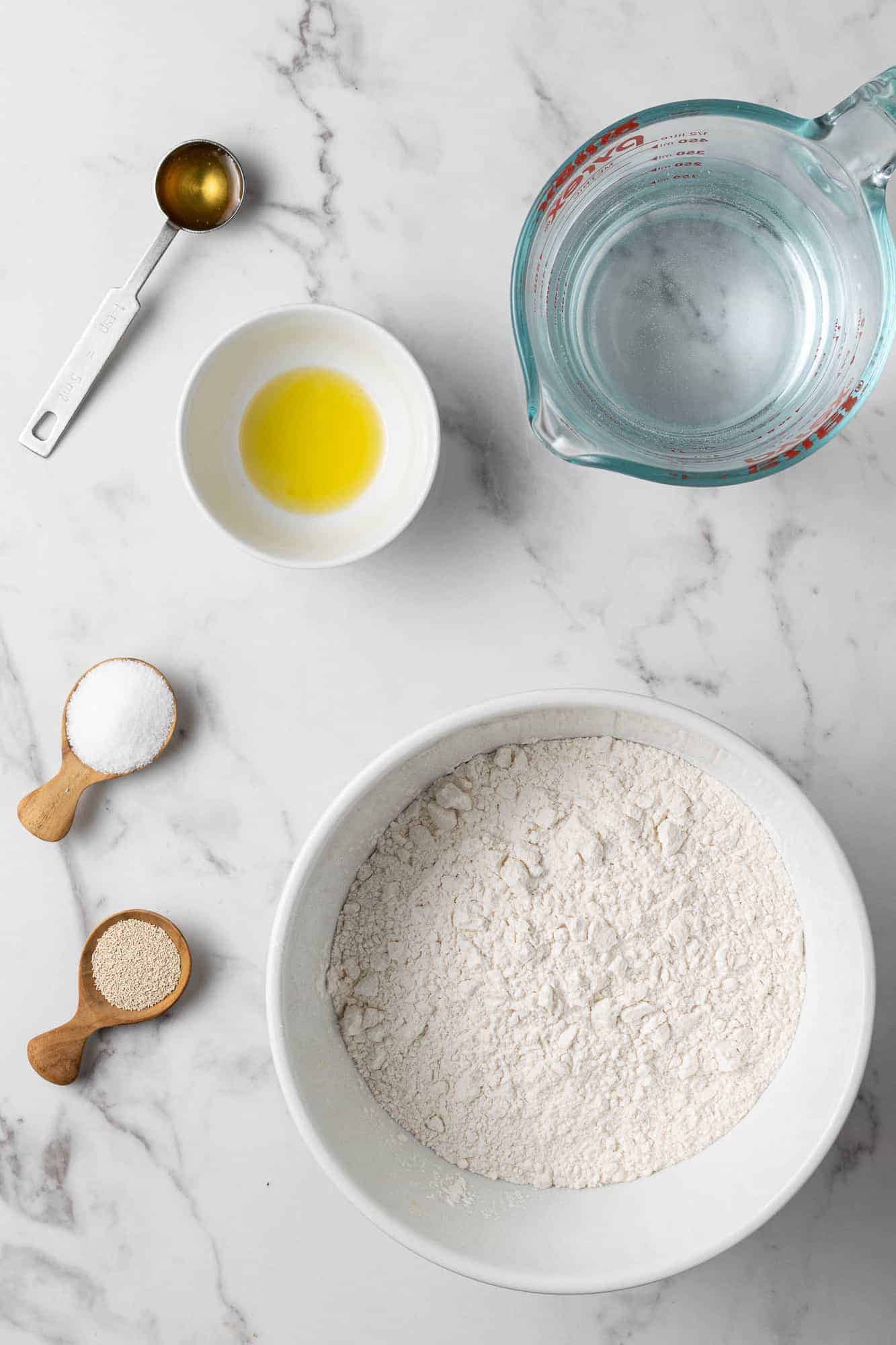 Overhead view of ingredients needed to make dutch oven bread: flour, oil, yeast, water, salt, honey.