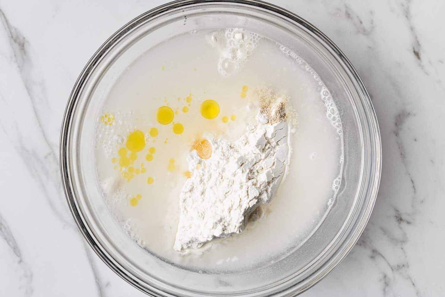 Unmixed bread dough ingredients in a glass mixing bowl.