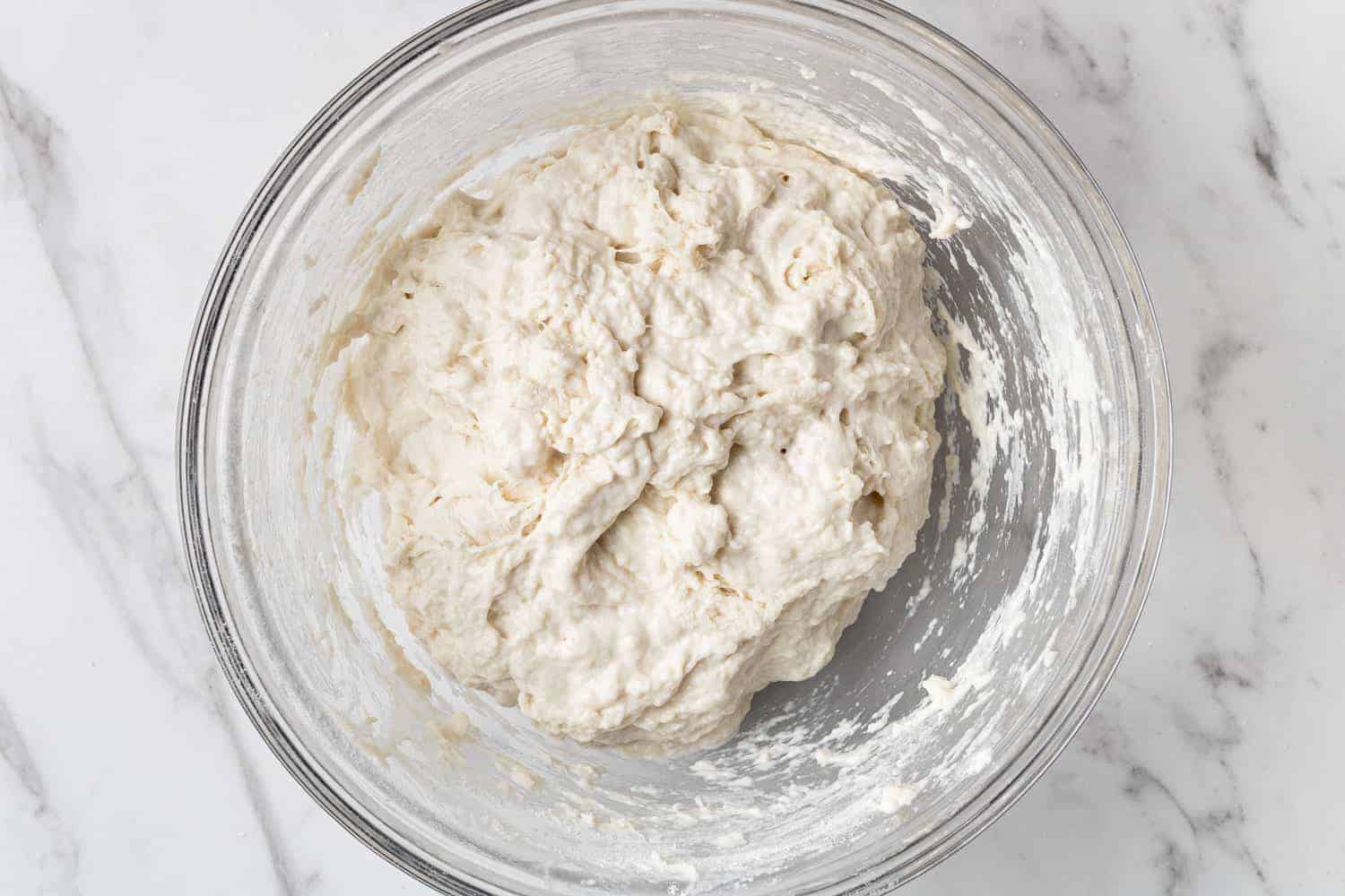 Bread dough in a clear glass mixing bowl.