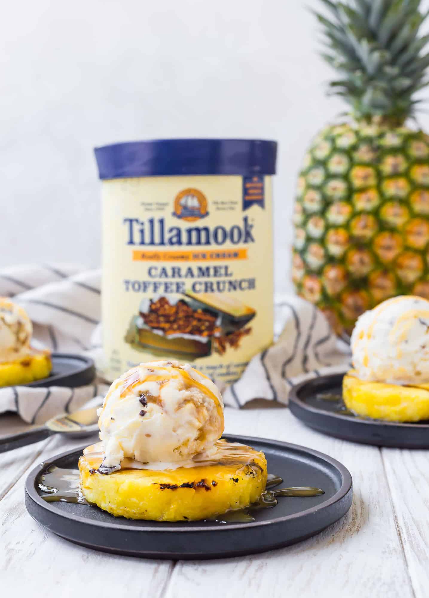 Grilled pineapple and ice cream in foreground, carton of ice cream in background.