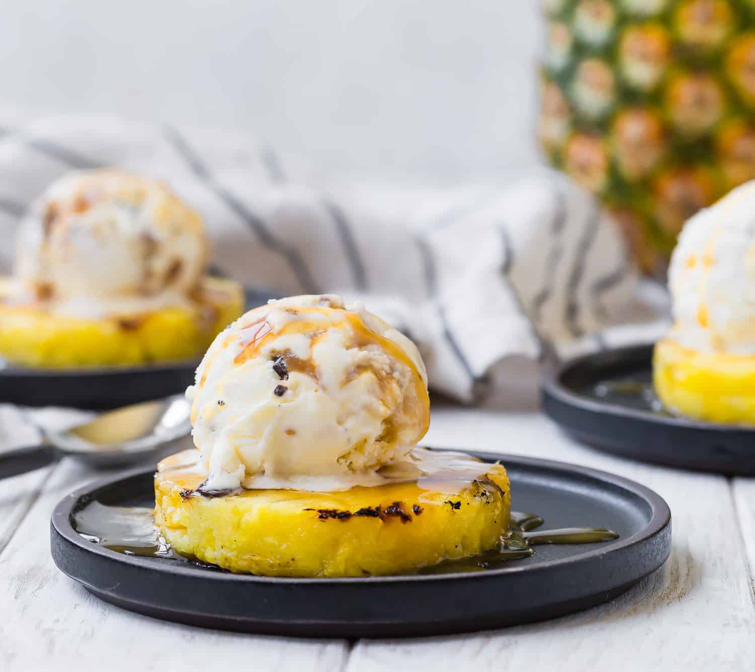 Grilled pineapple slice topped with ice cream. Additional servings in background.