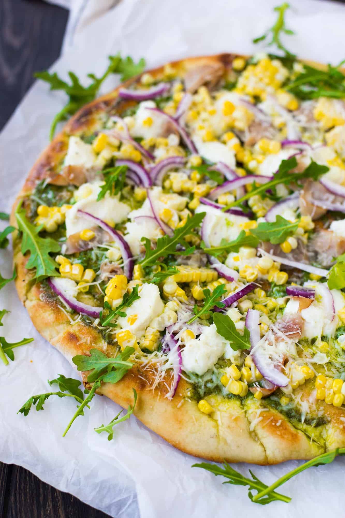 Grilled pizza on a piece of parchment, topped with ricotta cheese, arugula, and more.