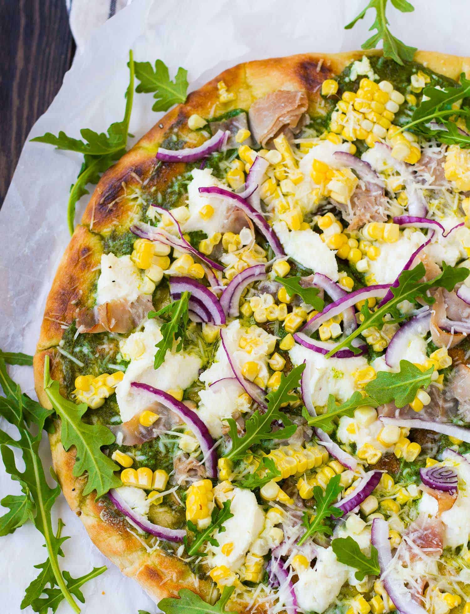Pizza on parchment with ricotta, red onion, arugula, and ham.
